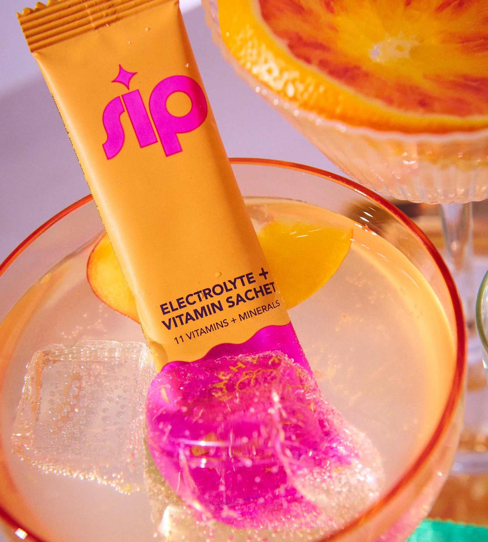 Sip Orange and pink electrolyte and vitamin sachet with a drink in the background